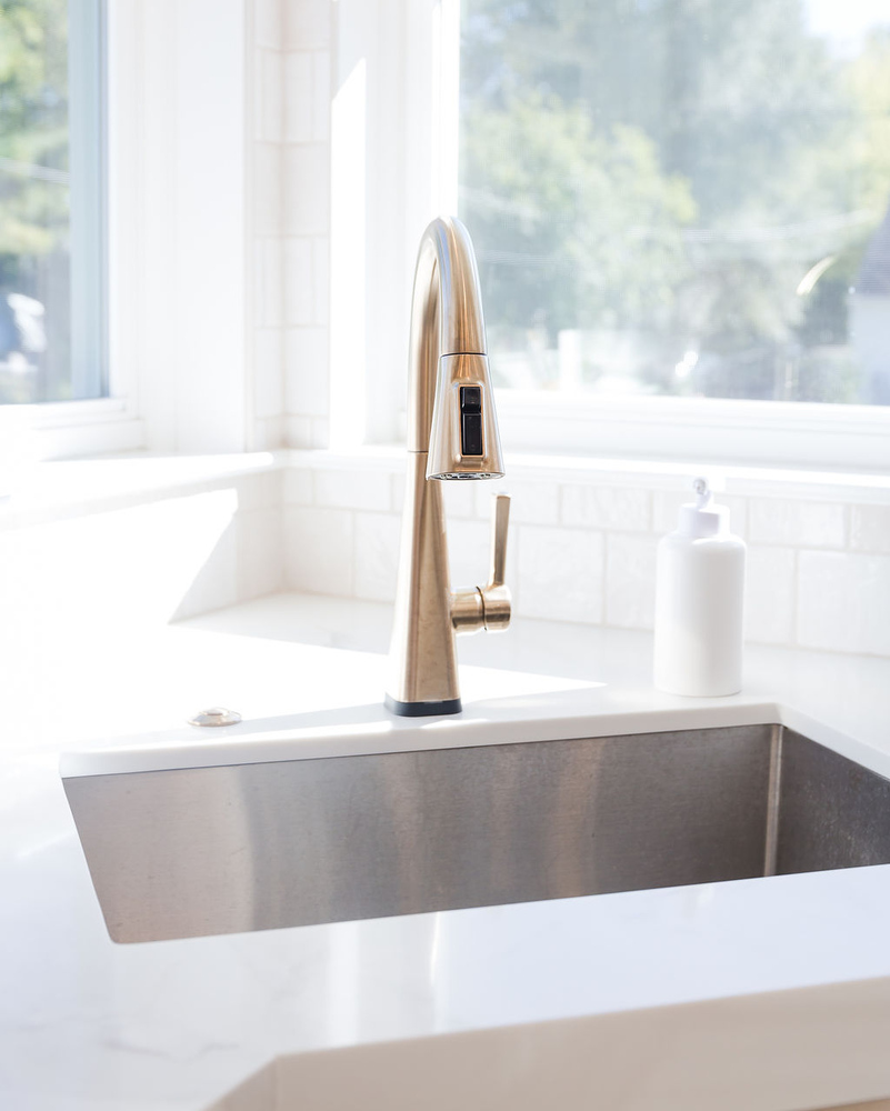 Brushed gold kitchen faucet over stainless sink designed by Cabinet Creations in Bloomfield Hills, MI