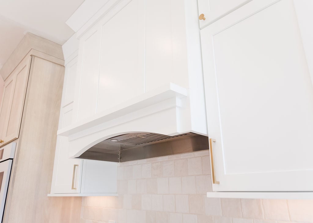 Custom white vent hood and cabinetry with brass handles by Cabinet Creations in Waterford Township, MI