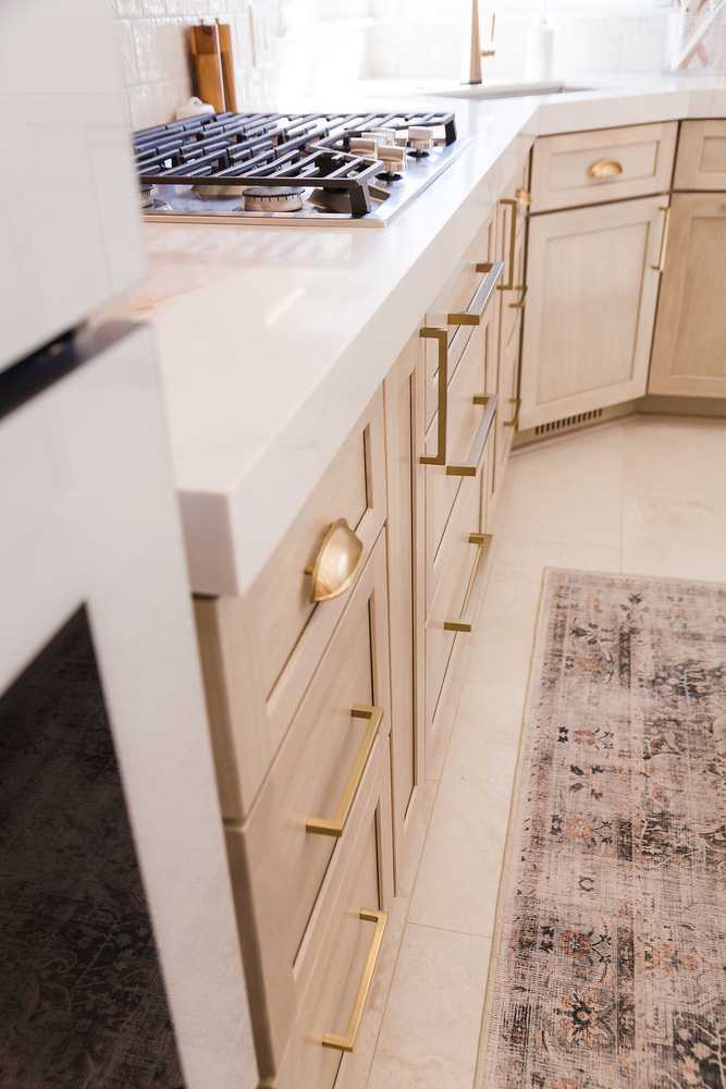 Elegant kitchen drawers with gold hardware beside cooktop in a Michigan custom home