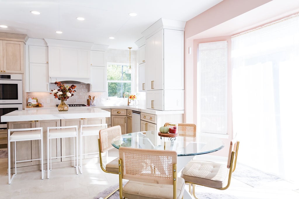 Elegant kitchen with white cabinetry, pink accent wall, and round glass dining table by Cabinet Creations in Bloomfield Hills, MI