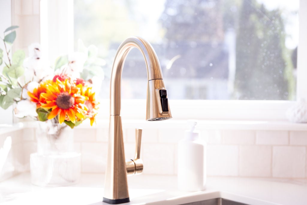 Gold pull-down kitchen faucet with bright window view designed by Cabinet Creations in Oakland County, MI