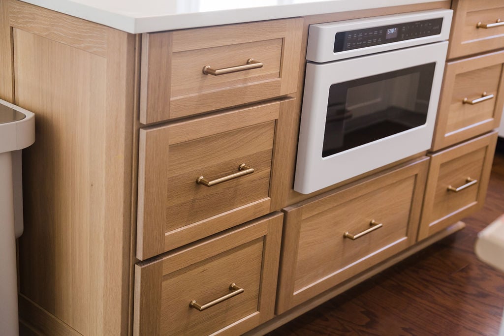 Light wood island cabinetry with built-in oven and brass handles by Cabinet Creations in Oakland County, MI