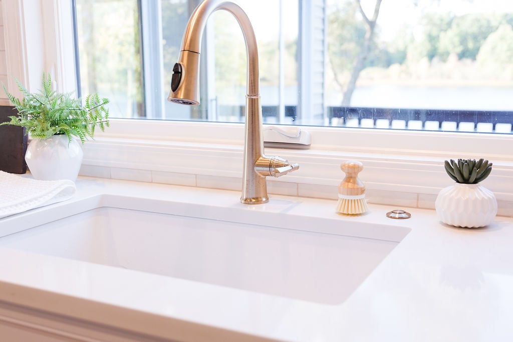 Modern kitchen sink with gold hardware and potted plants by Cabinet Creations in Michigan custom home