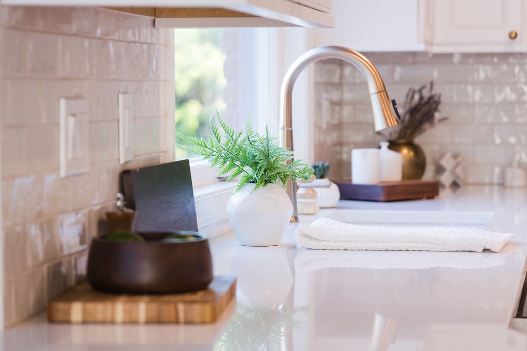 Side view of kitchen sink area with white quartz countertops and brushed brass faucet by Cabinet Creations in Michigan