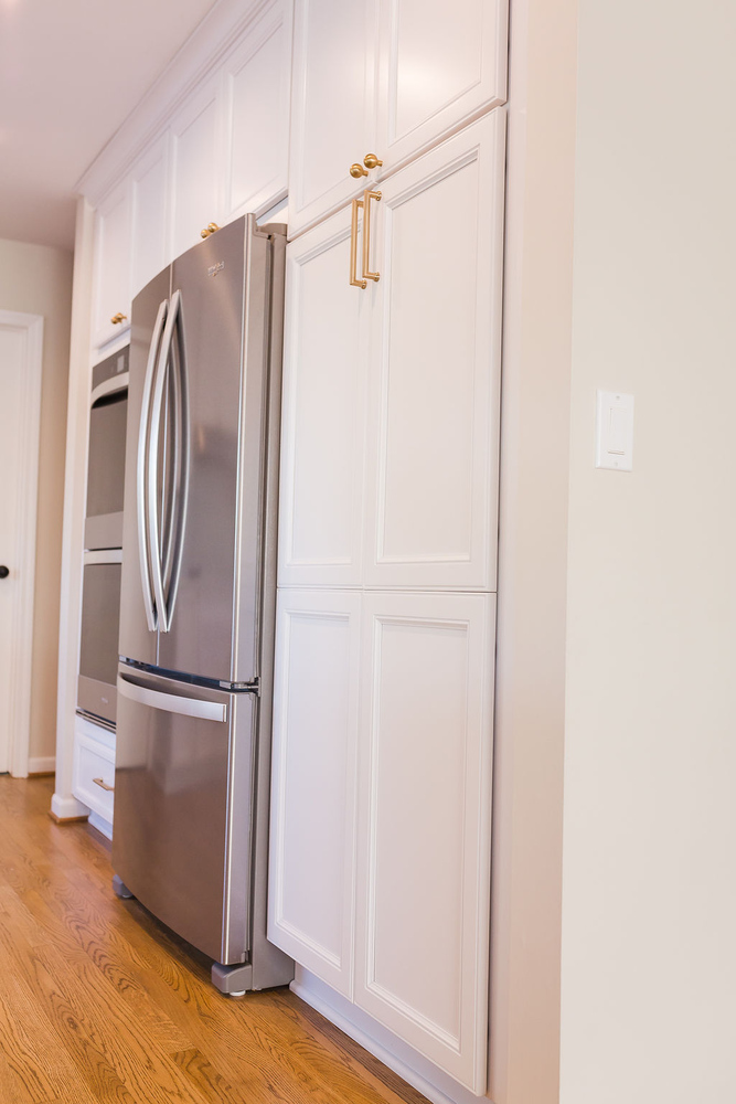 Tall white pantry cabinets beside stainless steel appliances in custom kitchen by Cabinet Creations, Oakland County, MI
