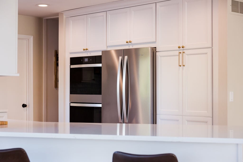 White quartz countertops and tall custom cabinetry surround stainless appliances in Oakland County kitchen by Cabinet Creations