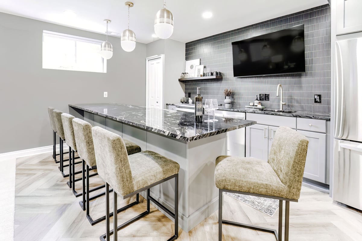 Custom bar island with upholstered stools in Clarkston basement by Cabinet Creations