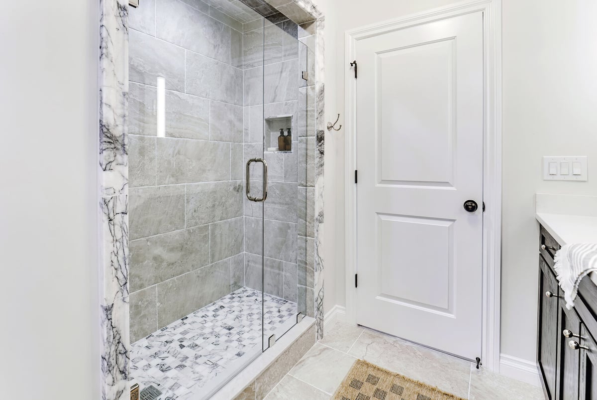Frameless glass shower with marble accents in Clarkston basement bath by Cabinet Creations