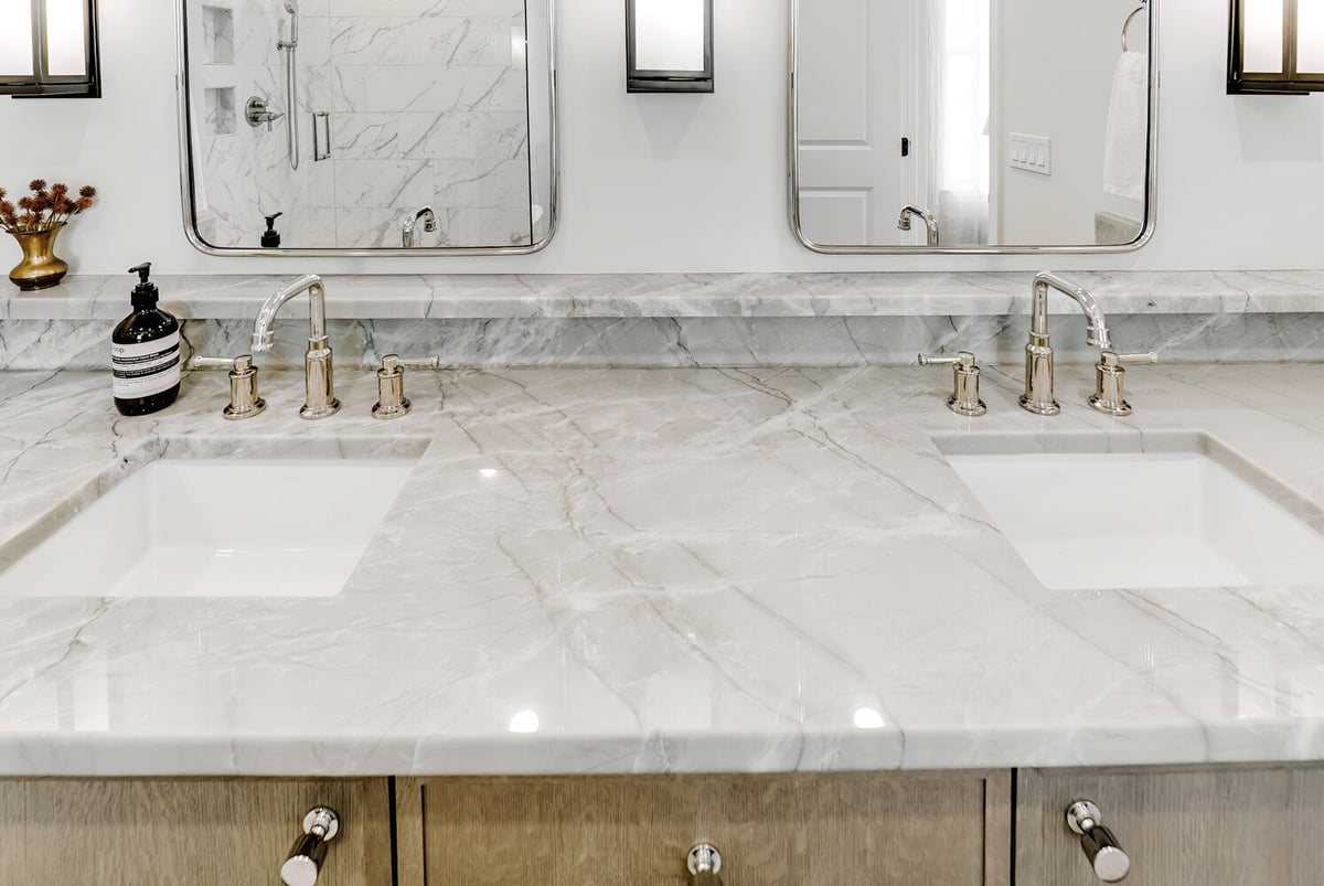 Close-up of dual-sink marble vanity with polished chrome fixtures in a custom home bath by Cabinet Creations