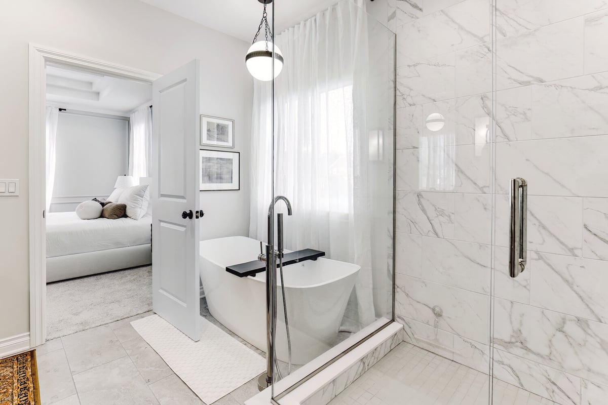 Freestanding bathtub next to glass-enclosed marble shower in a custom home by Cabinet Creations in Oakland County