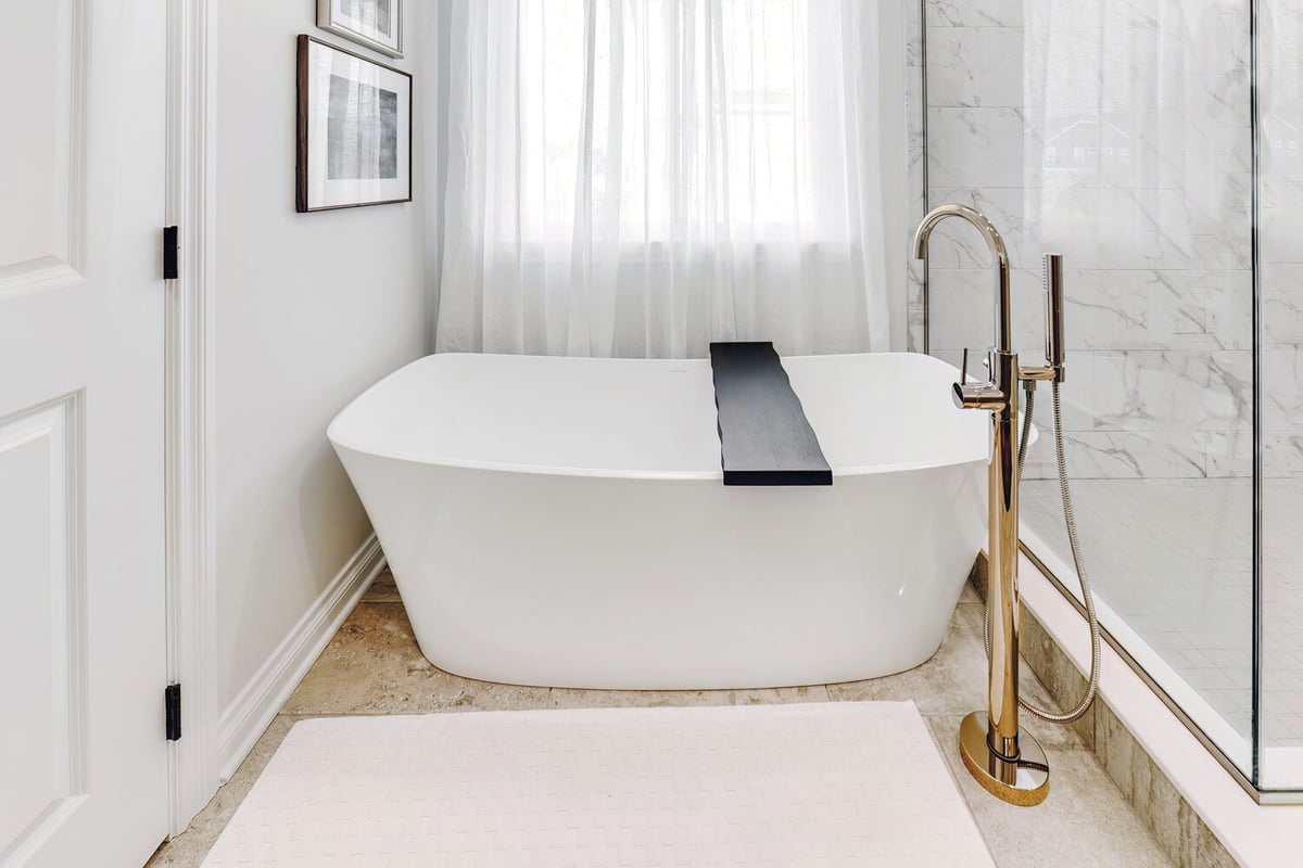 Freestanding soaking tub with chrome floor-mount faucet in a Waterford Township custom home by Cabinet Creations
