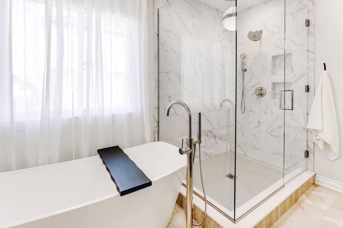 Glass-enclosed walk-in marble shower next to a soaking tub in a custom master bath by Cabinet Creations in Waterford, MI