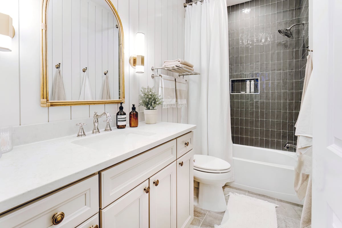 Elegant bathroom remodel in Clarkston by Cabinet Creations featuring gold mirror and vertical shower tile
