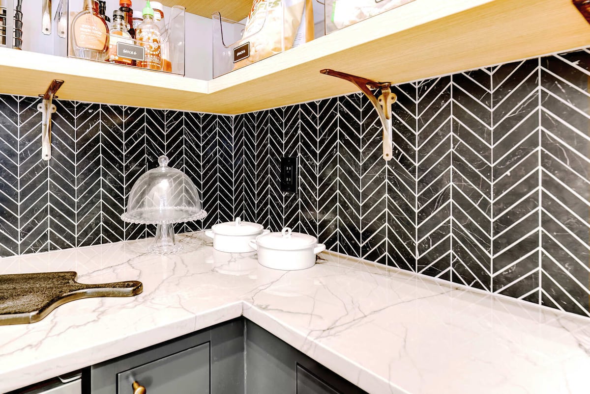 Marble countertop with glass cake dome and chevron backsplash in a custom pantry by Cabinet Creations, Oakland County, MI