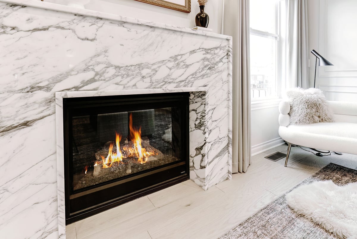 Marble fireplace with glowing flames and neutral living room décor by Cabinet Creations in Oakland County, MI