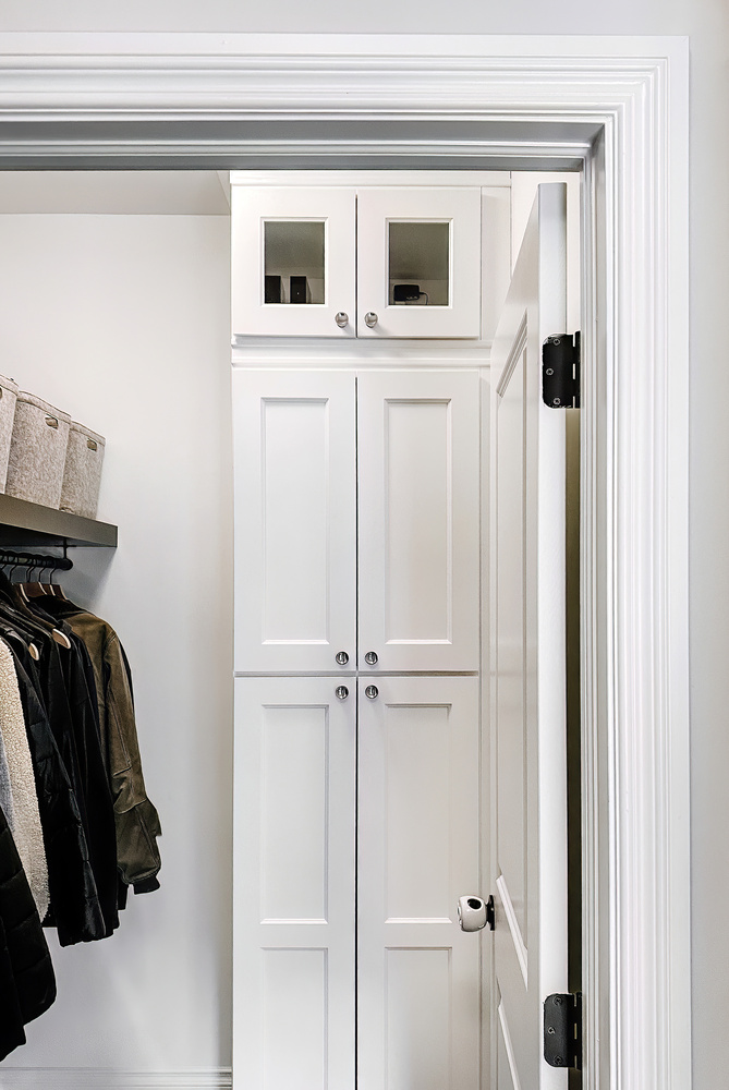 Custom white cabinetry with glass upper doors in a mudroom closet by Cabinet Creations in Oakland County, MI