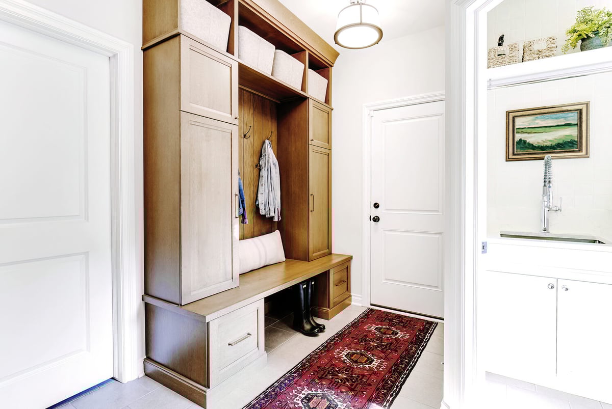 Mudroom bench and coat storage design with wood cabinets and Persian-style rug by Cabinet Creations in Waterford Township
