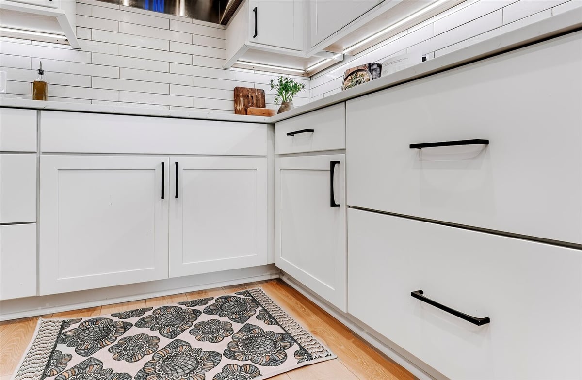 Lower white cabinets with black hardware and floral rug in a Michigan kitchen by Cabinet Creations