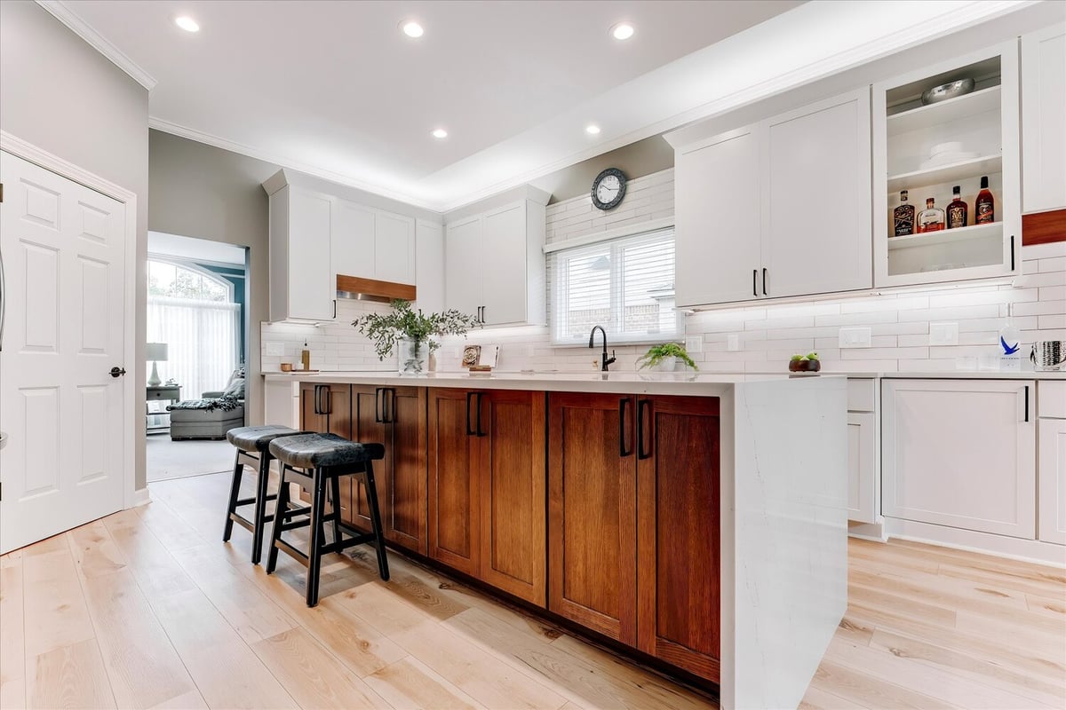 Two-tone kitchen island with white quartz top and black leather stools by Cabinet Creations in Michigan