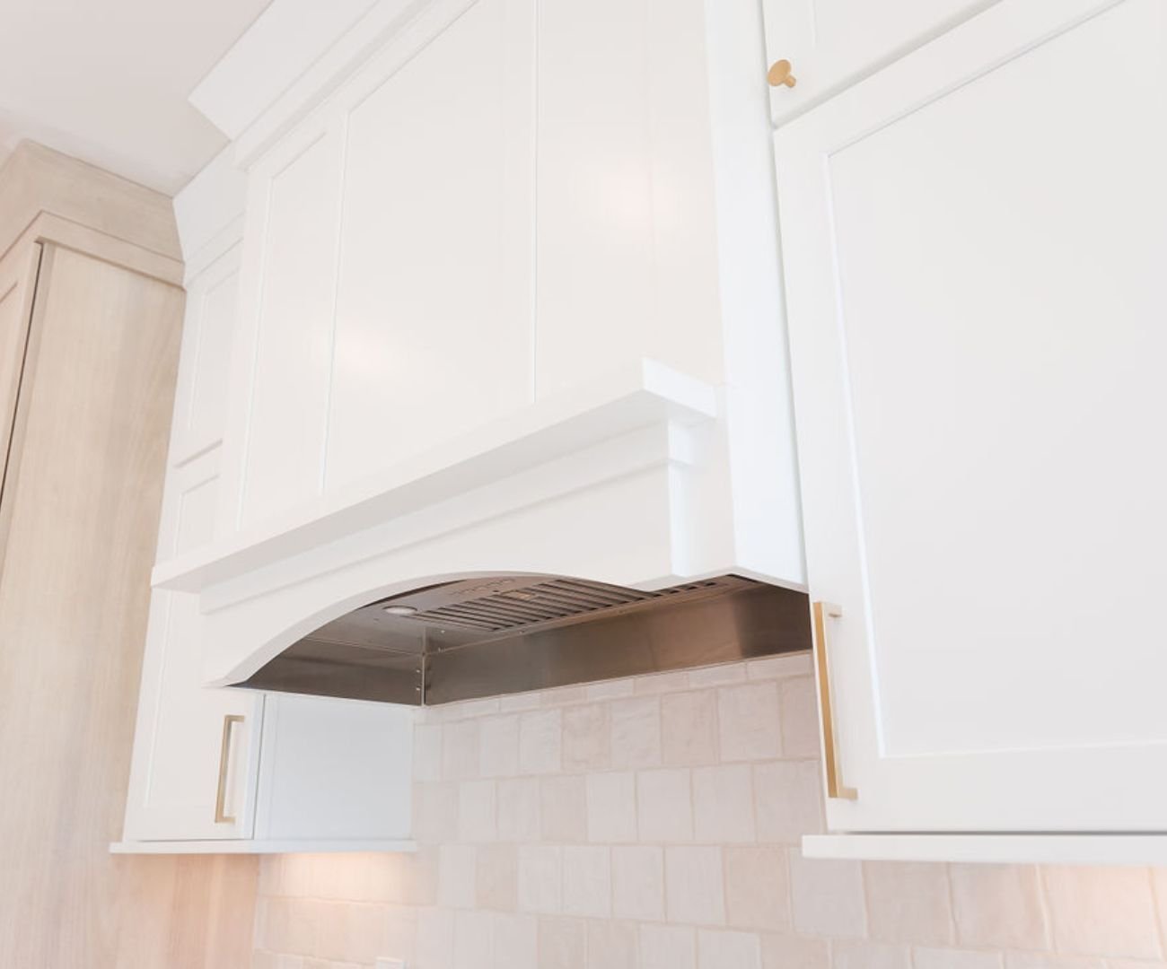 A custom-built hood vent with a white tile backsplash below by Cabinet Creations in White Lake Township, MI