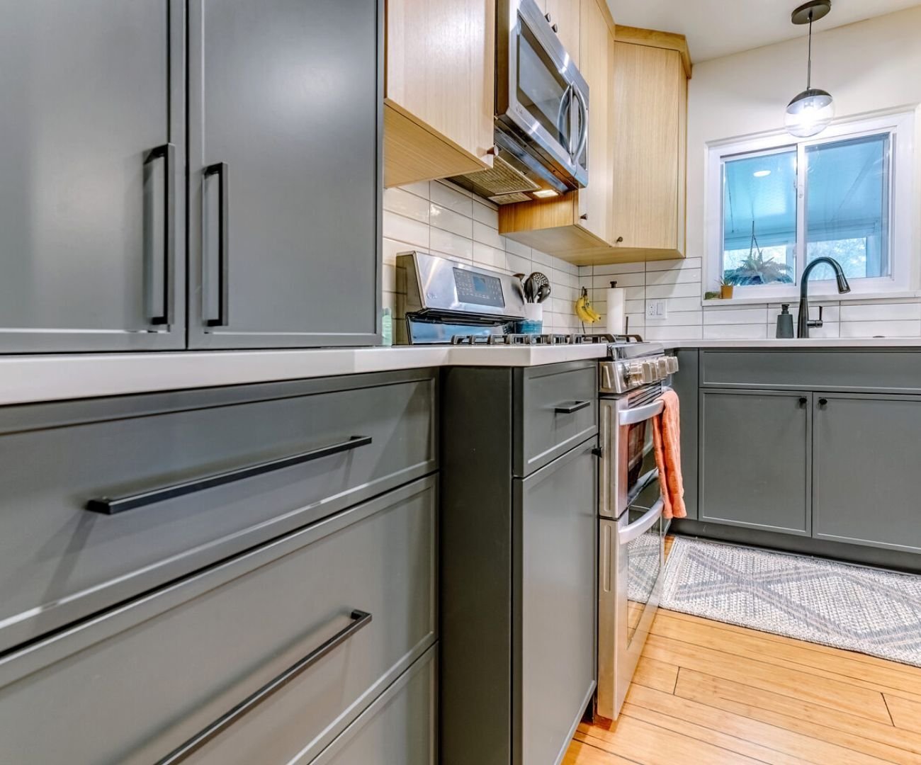 Black cabinet hardware matches the faucet, contrasts against the light wood cabinetry, and blends naturally into the dark gray lower cabinets.