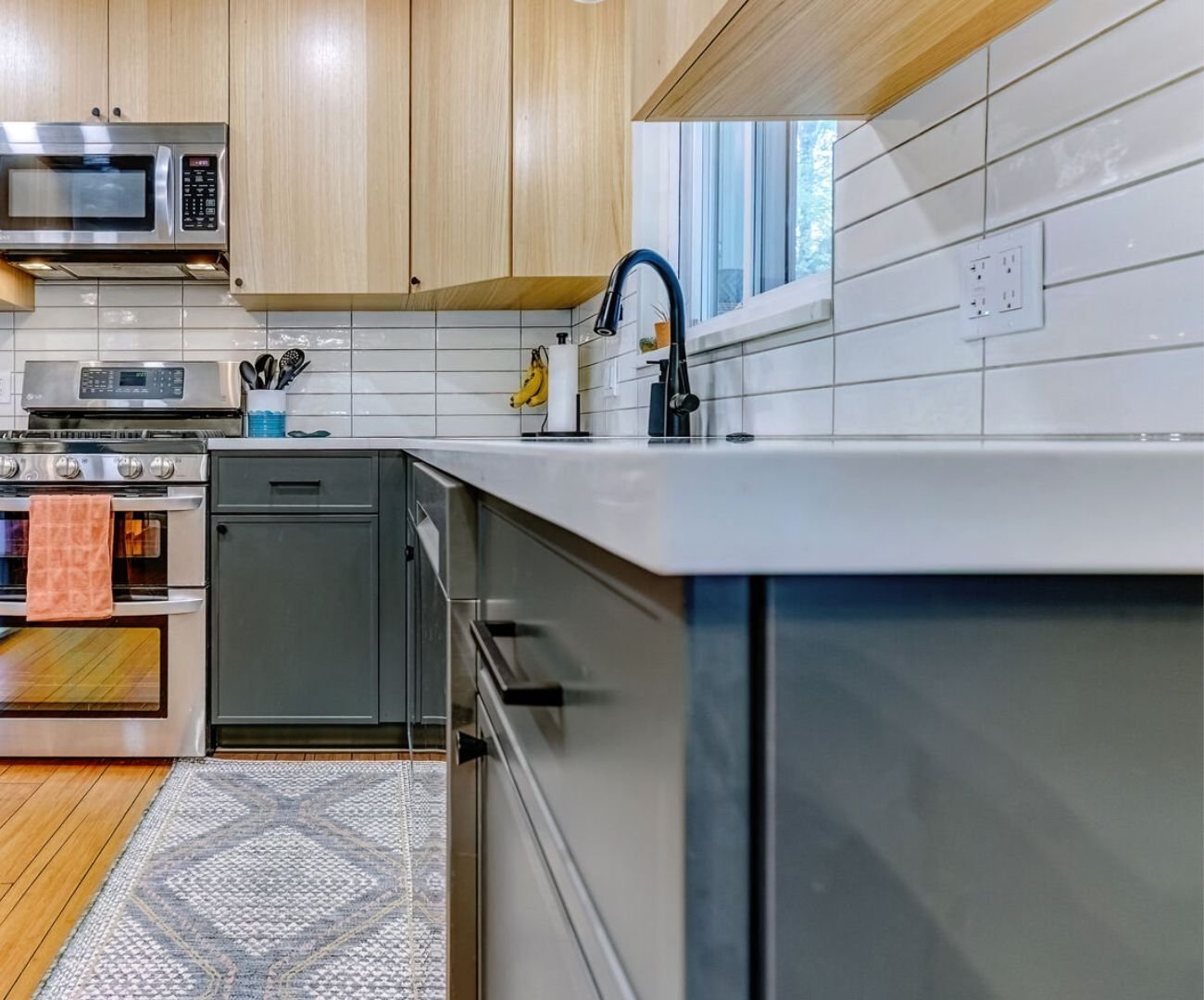 Low-angle view of modern custom kitchen in Clarkston, MI featuring a white tile backsplash, sleek drawers, and stove by Cabinet Creations