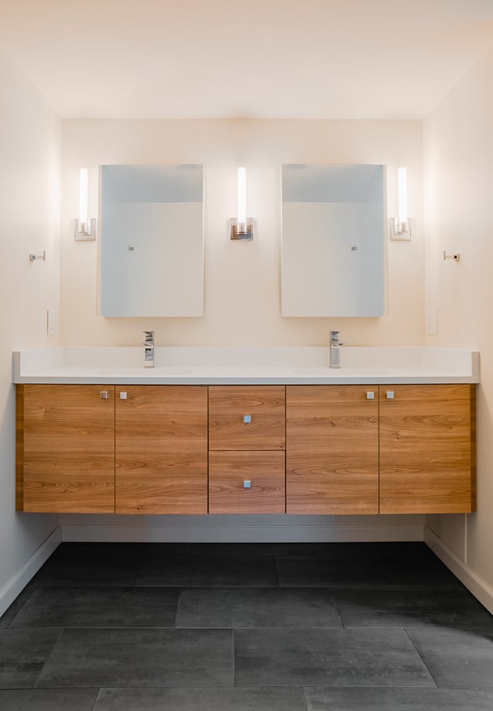 Modern double vanity bathroom remodel by Cabinet Creations in Birmingham, MI featuring sleek wood cabinets and minimalist lighting